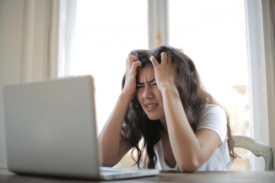 Student holds their head in their hands in a stressed manner in front of a laptop.