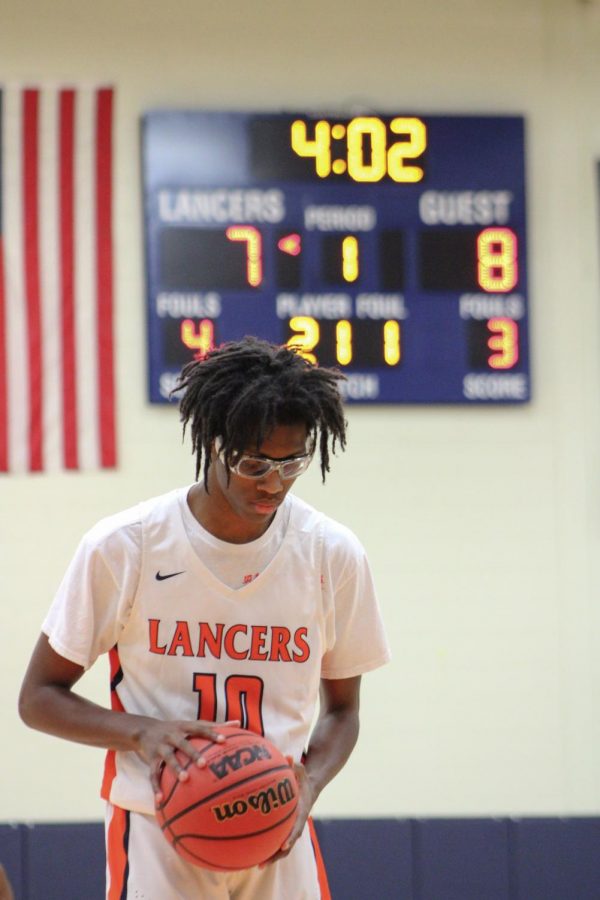 A basketball player holding a basketball on the court in front of a scoreboard